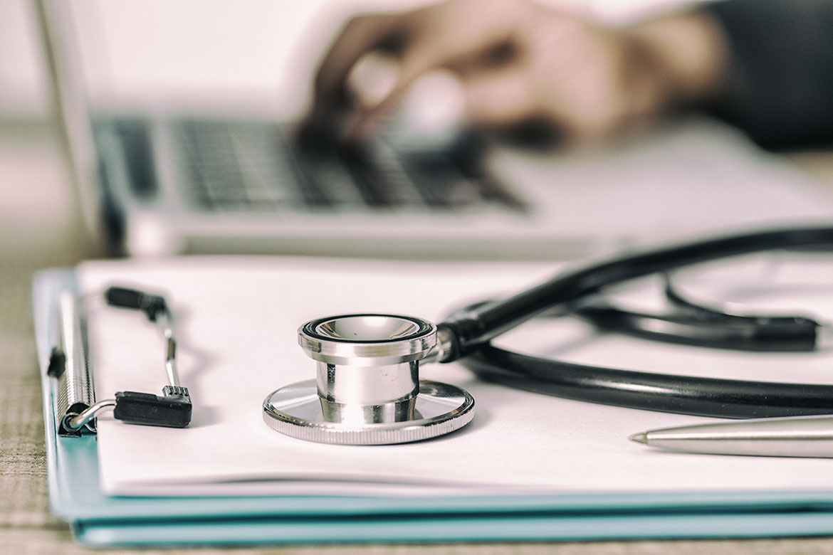 Stethoscope with clipboard and laptop on desk