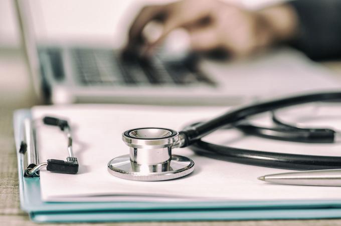 Stethoscope with clipboard and laptop on desk