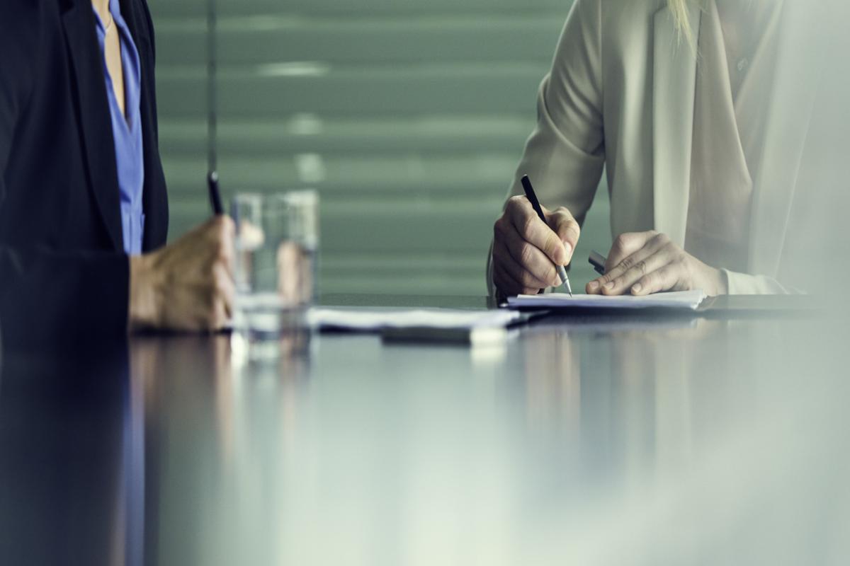 Two people at a meeting, writing with glasses of water in front of them