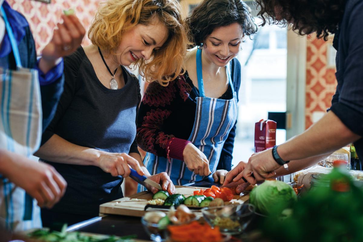 People gathered around a cutting board of fresh vegetables
