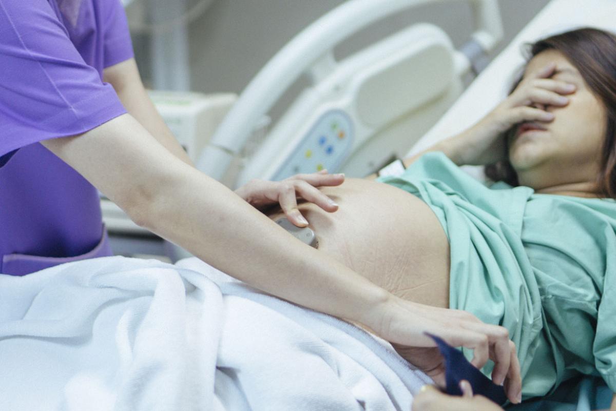 A pregnant woman covering her face while a health care worker attends to her