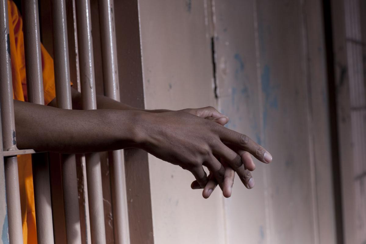 A prisoner stands with hands hanging outside the cell