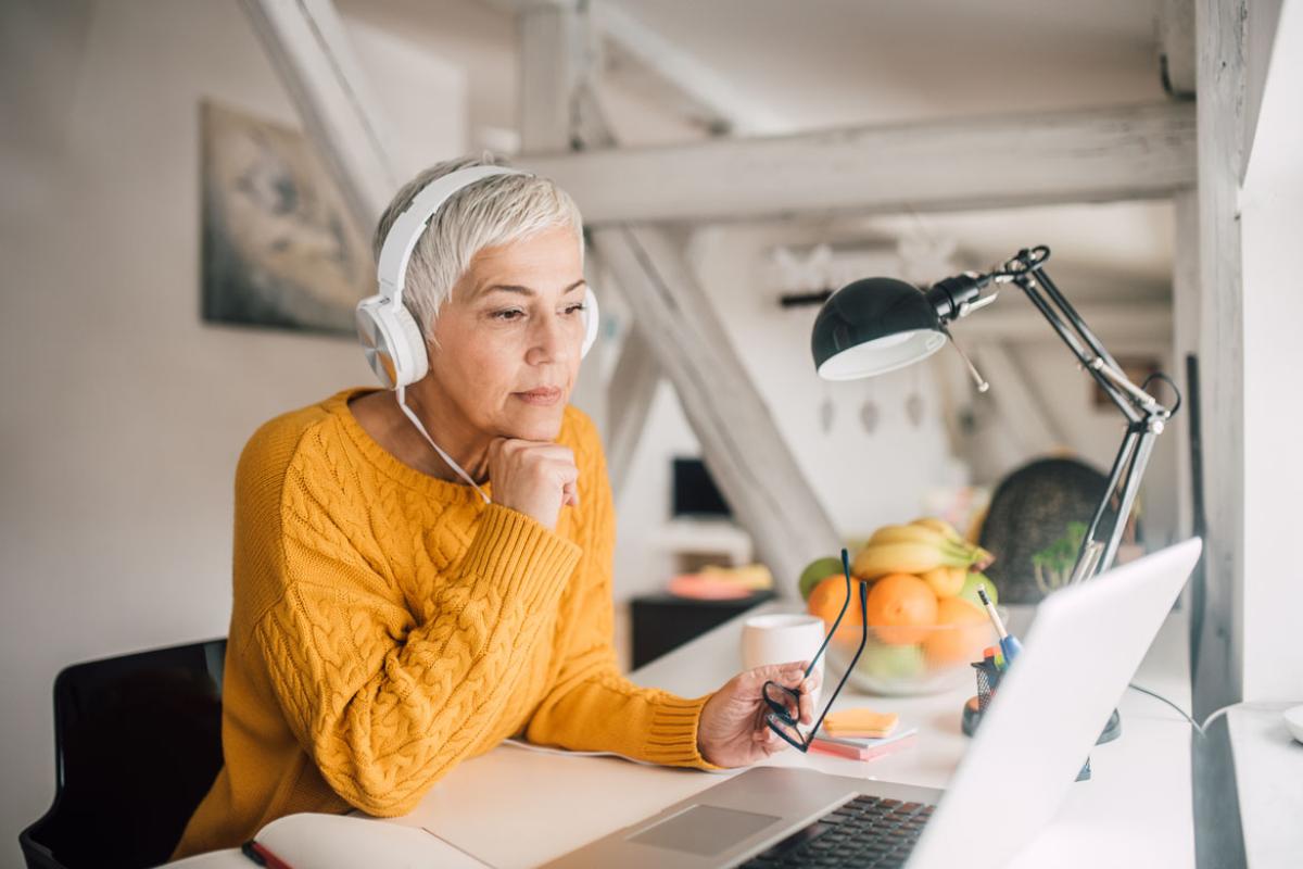 A woman wearing headphones while viewing her laptop