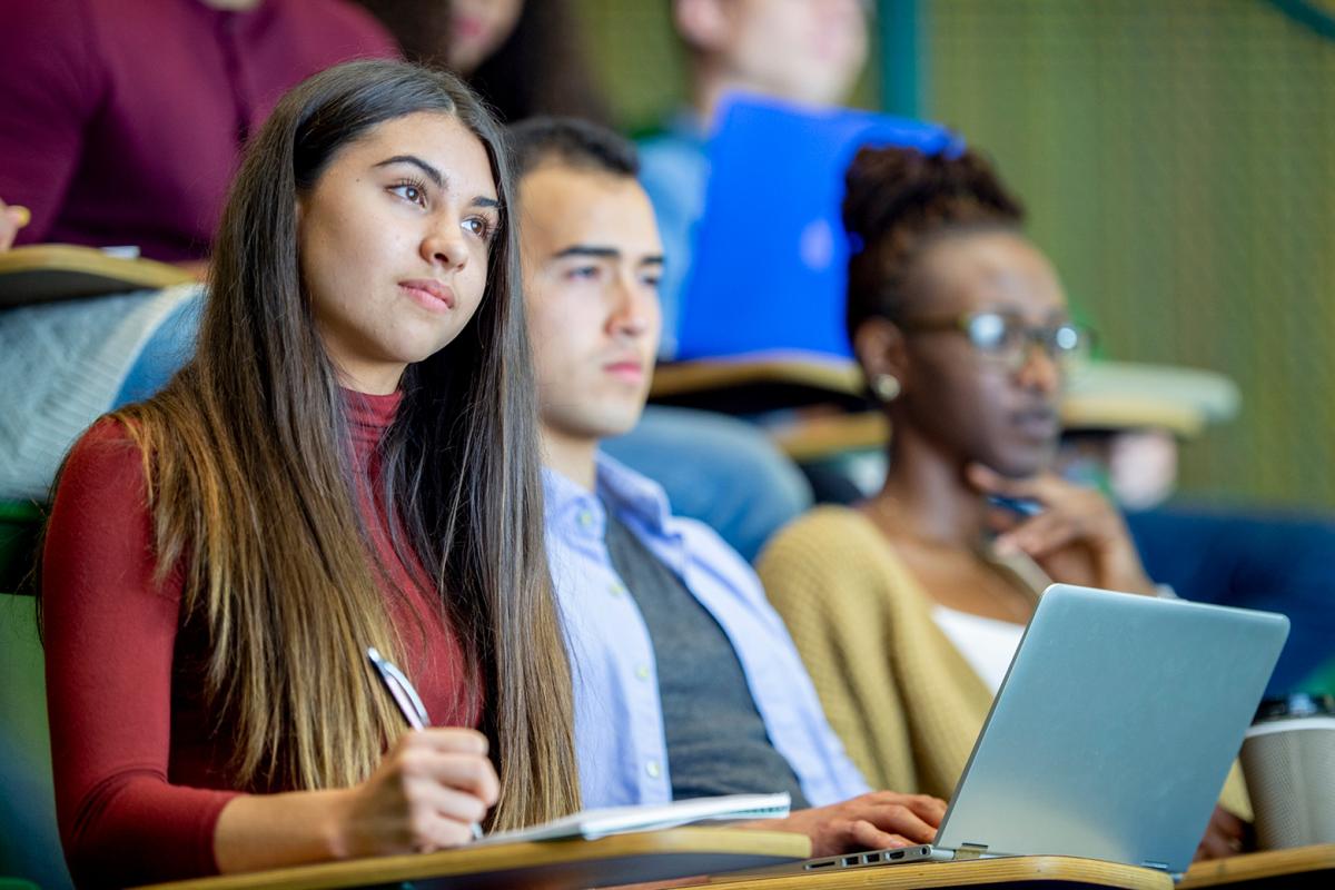 Three students taking notes in a lecture hall
