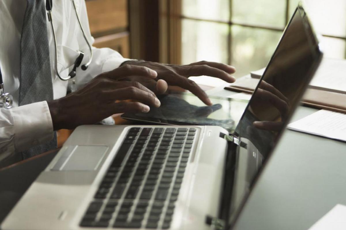 Hands working on a tablet next to a laptop