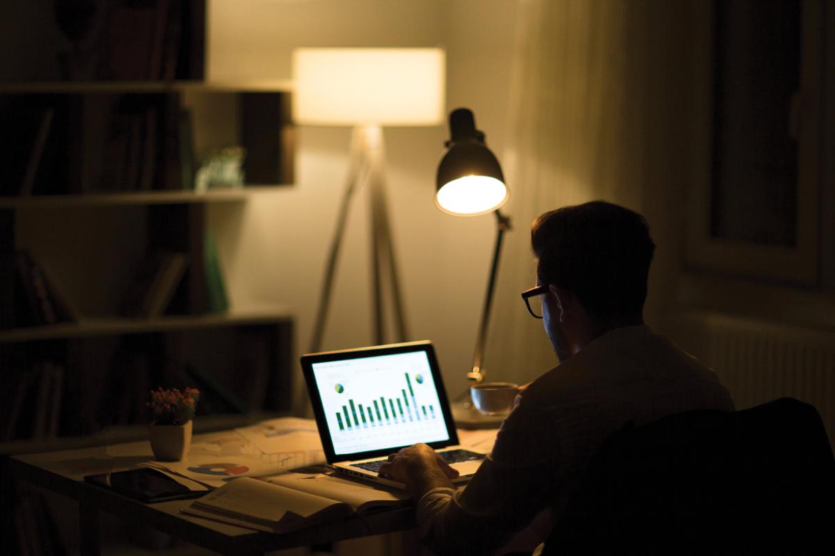 Man in a darkened room in front of computer screen displaying data bars