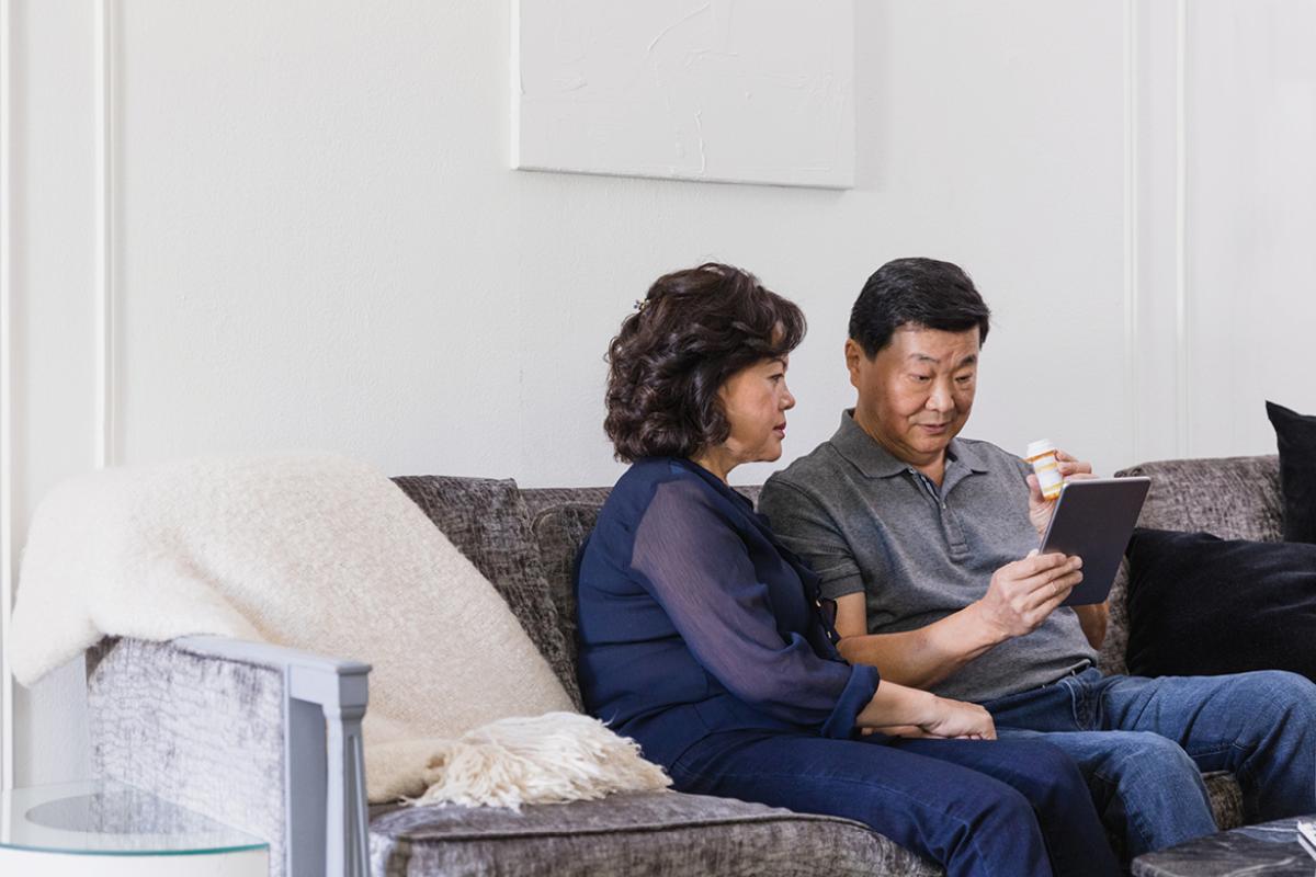 Man and woman sitting on a sofa with an iPad, medicine bottle in man's hand