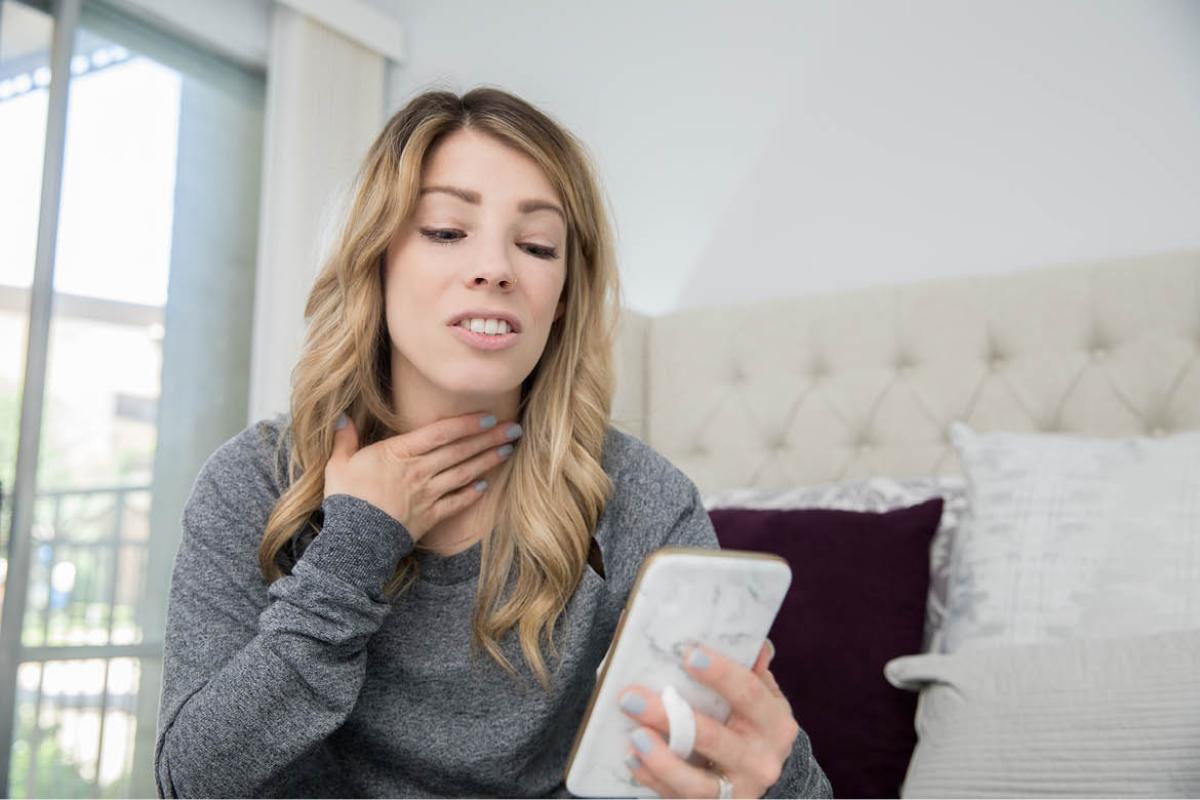 Woman holding throat and looking at smartphone
