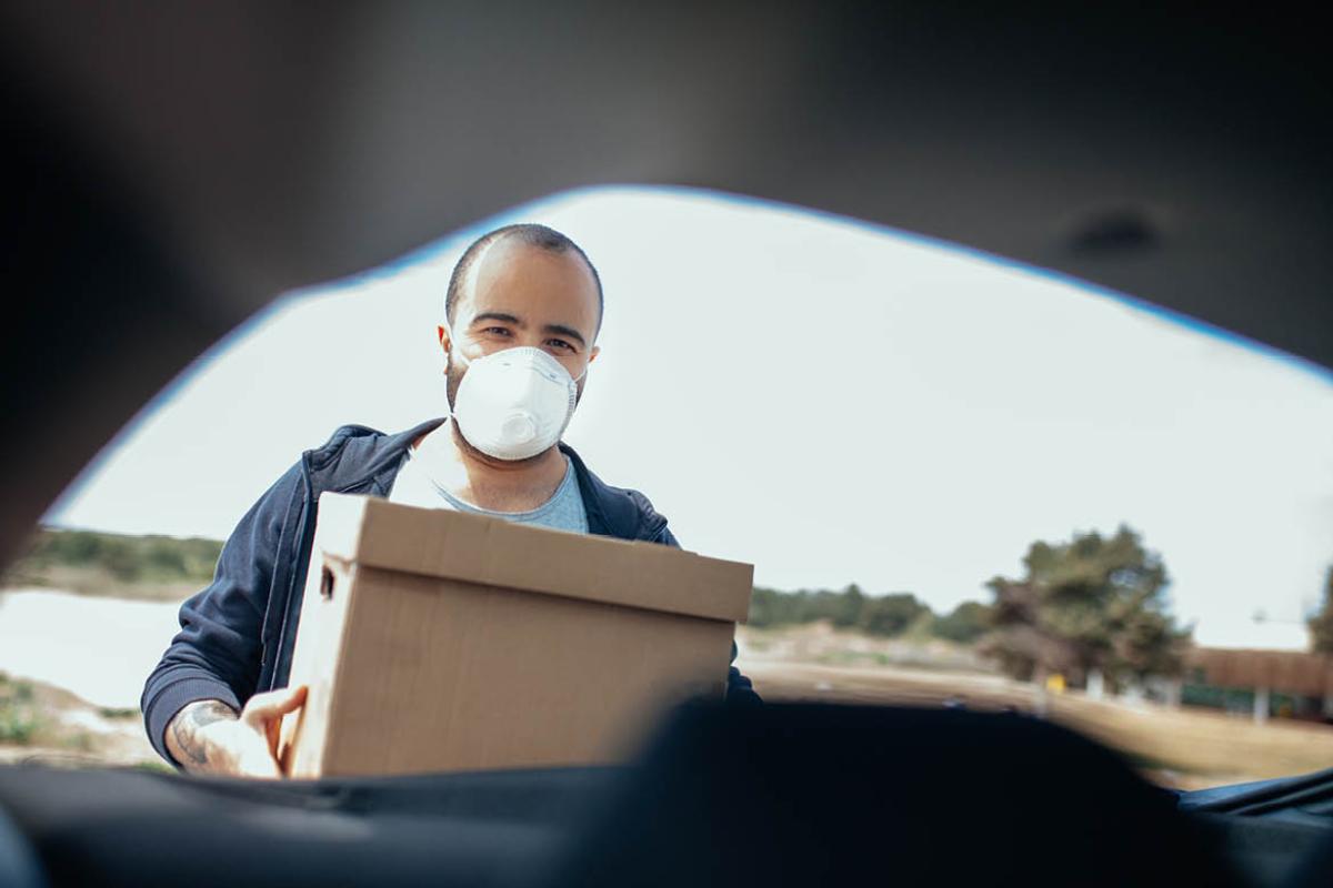 Person wearing facemask and holding a box