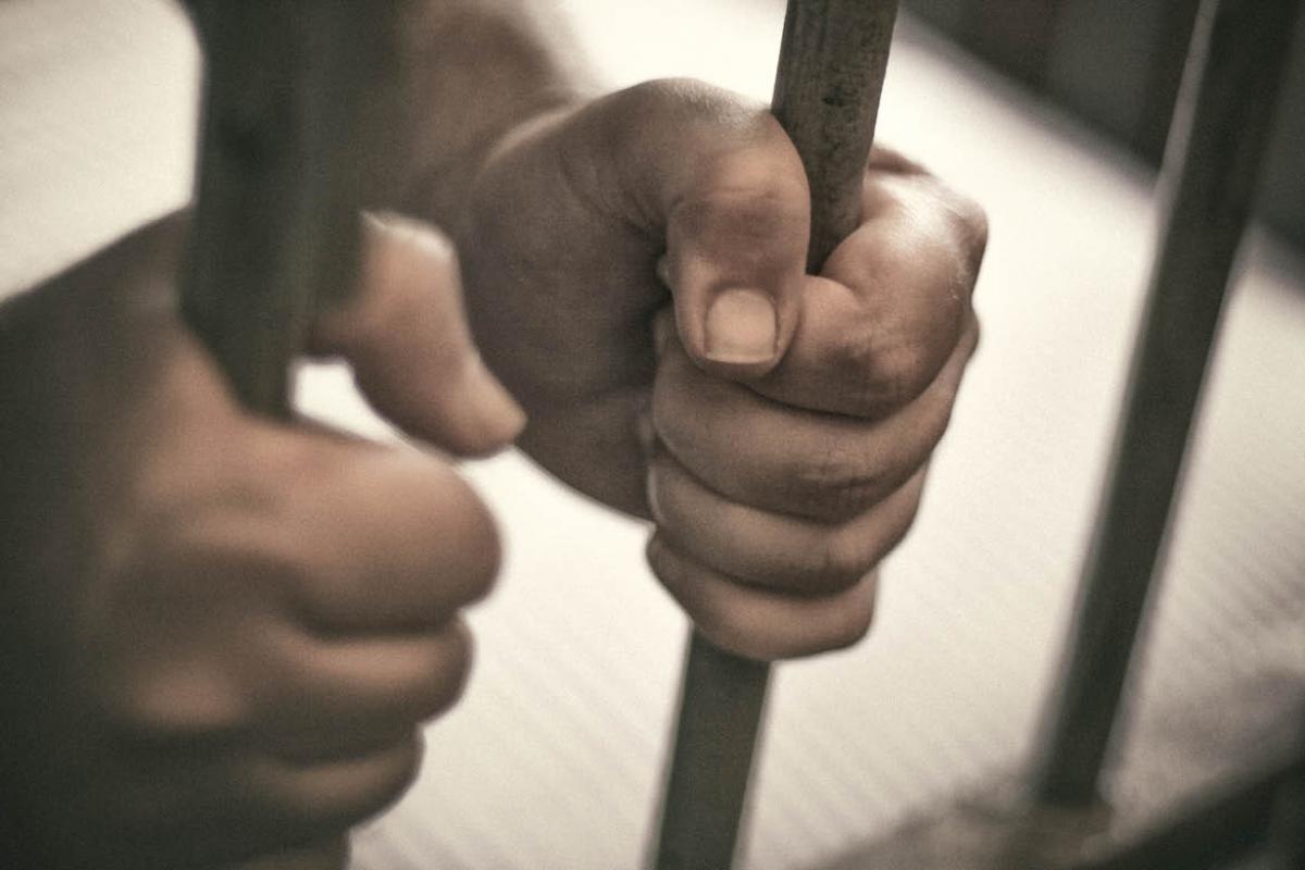 Hands holding prison cell bars