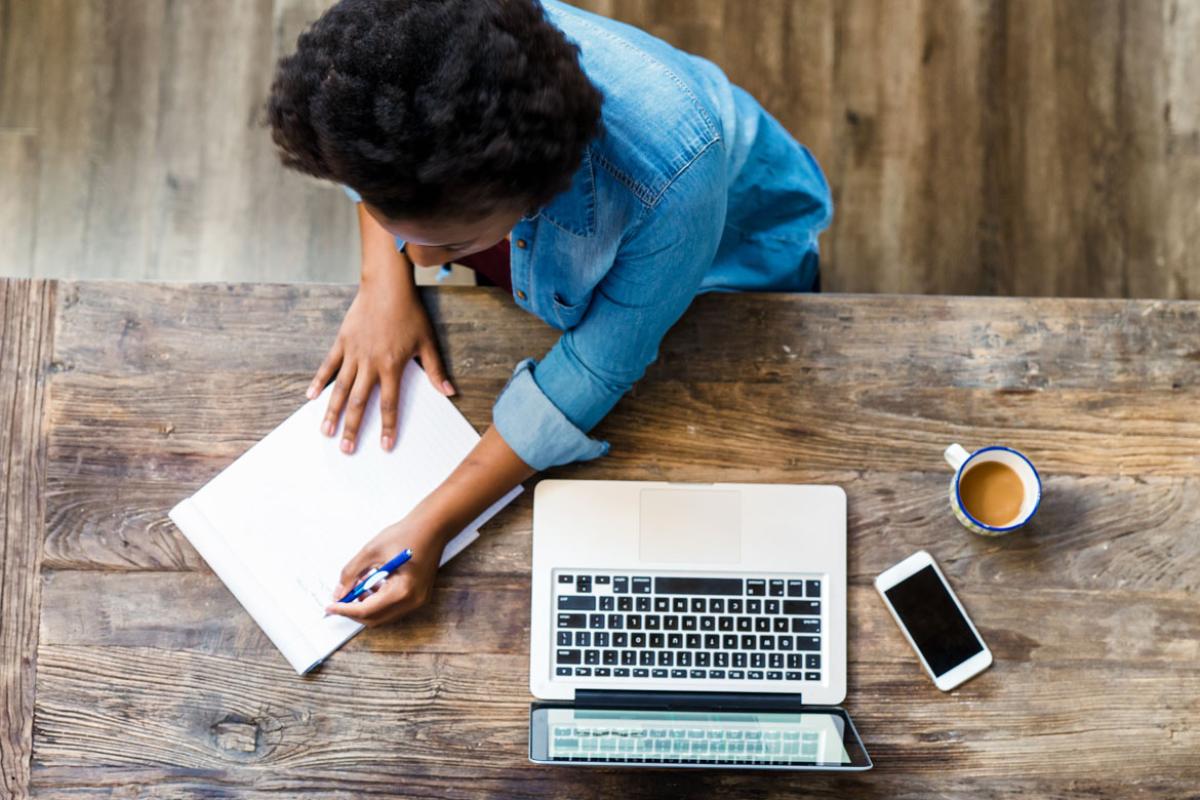 Person writing at a desk with a laptop