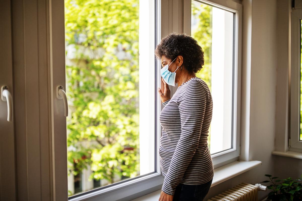 Woman in face mask looking out a window
