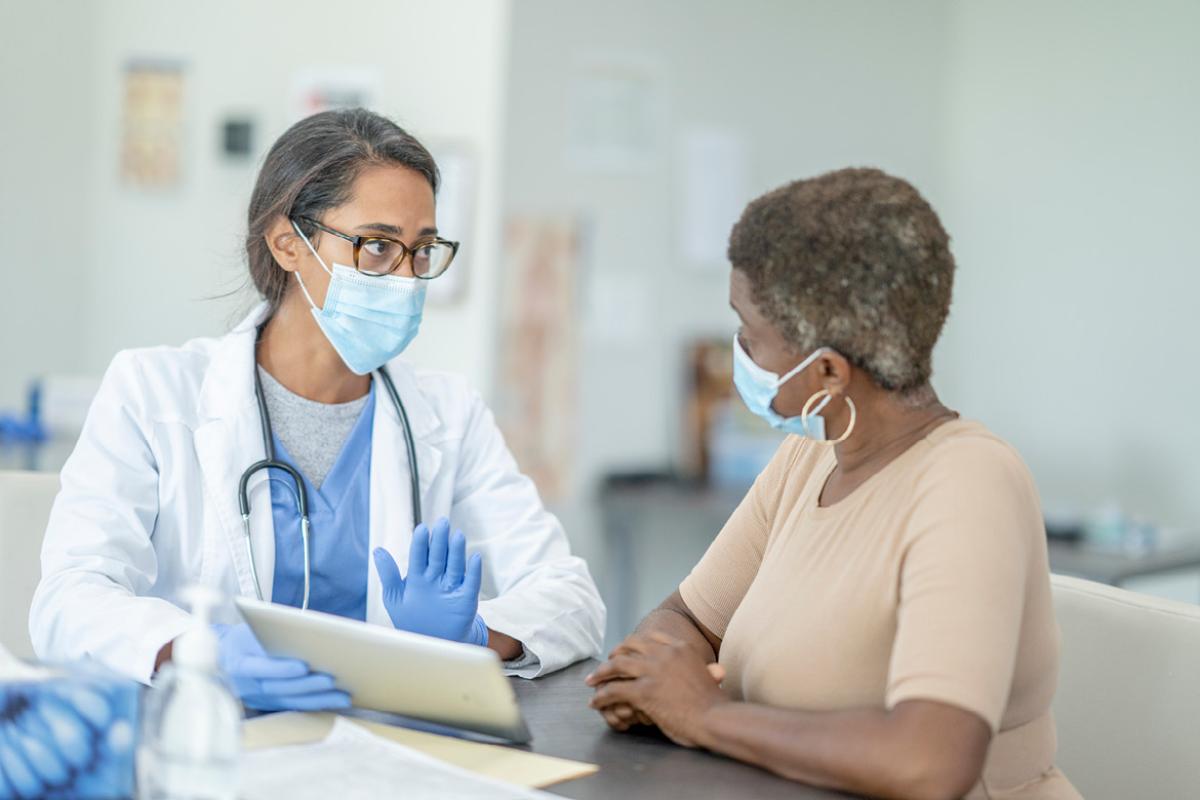 Doctor consulting patient, both wearing PPE.