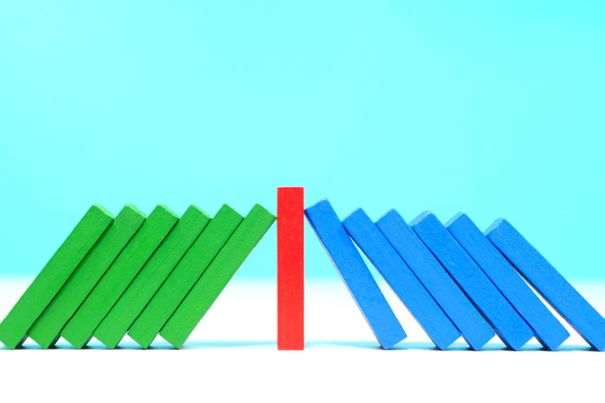 A stack of green blocks leaning against a single red block on one side and a stack of blue blocks leaning against the other side of the red block..