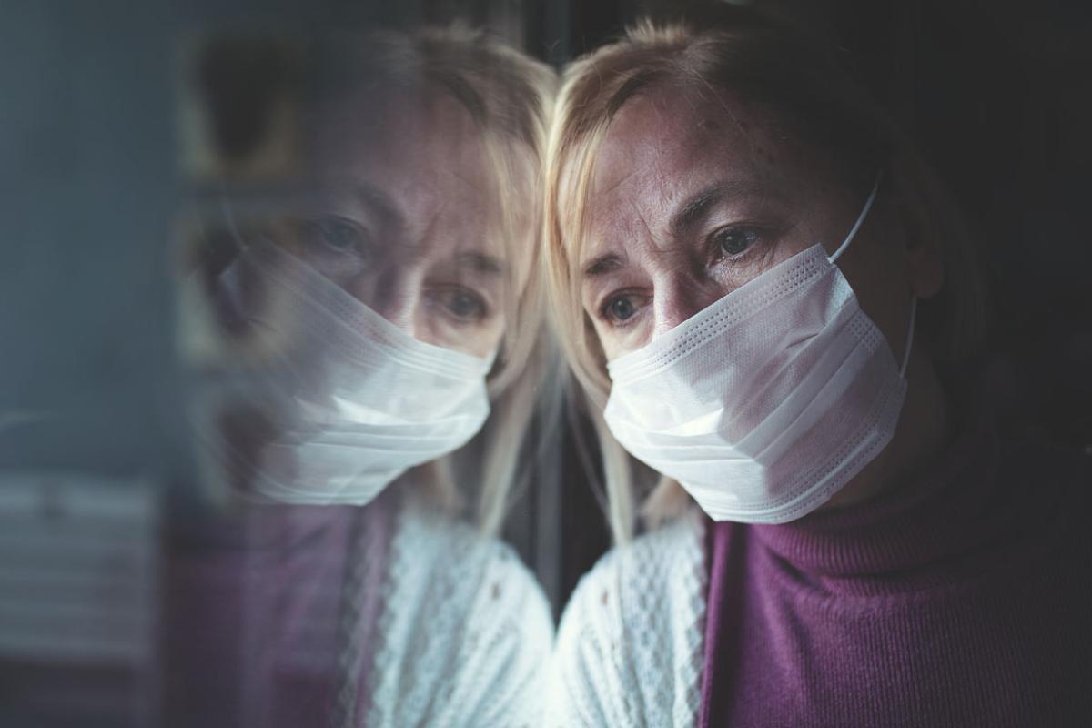 Person in a face mask looking out a window