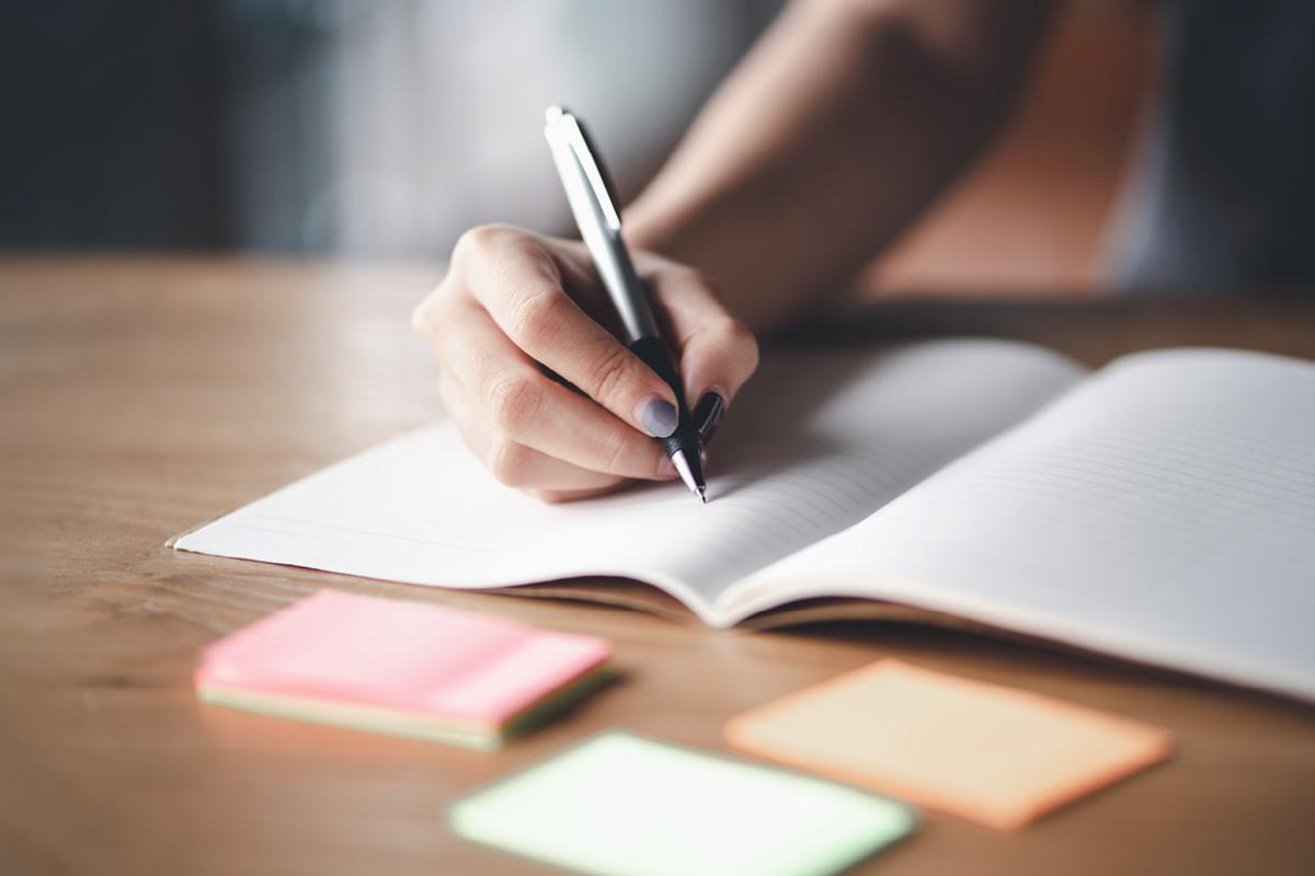 Close-up of a hand writing in a notebook with a pen.