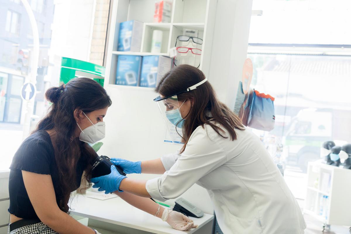 Doctor wearing PPE taking the blood pressure of a patient wearing a face mask.
