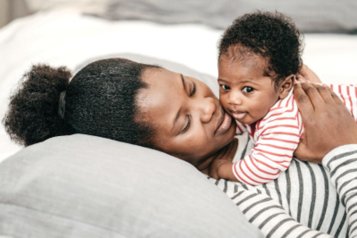 African-American woman holding a baby on her chest as she lays down.