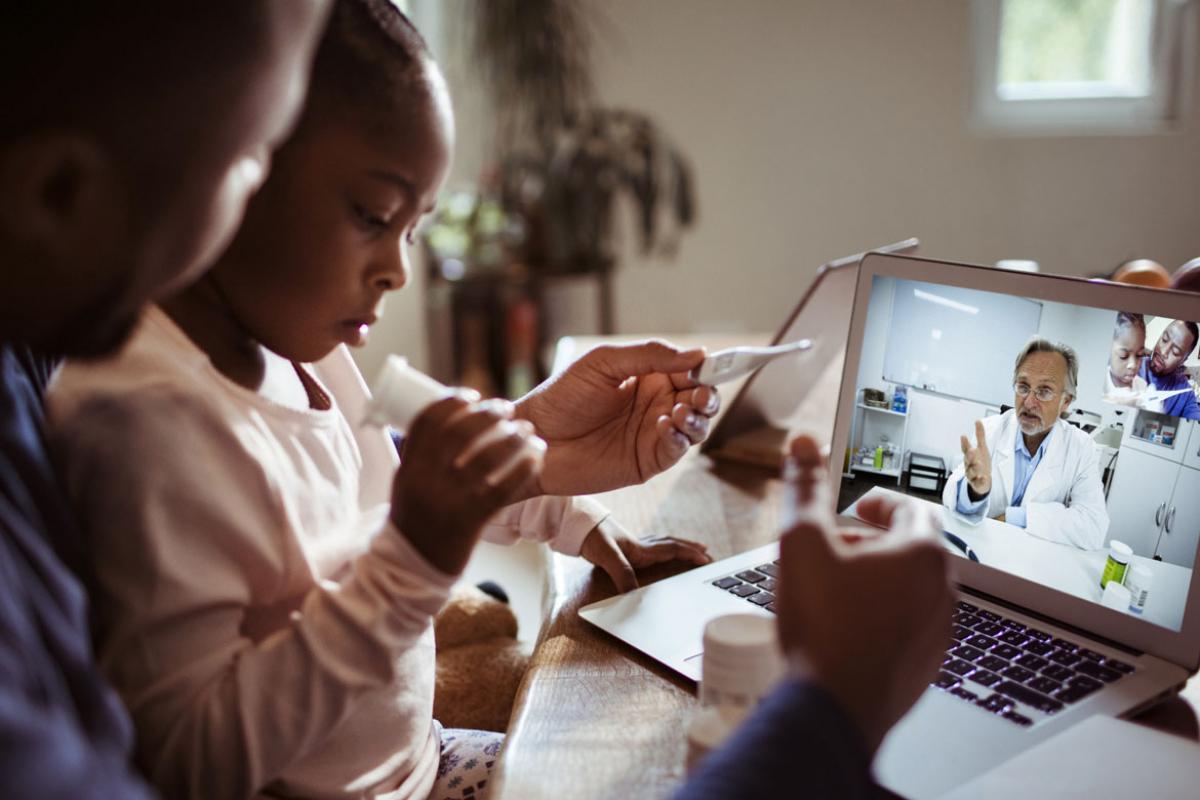 Parent and child speaking with a doctor through a telemedicine session on a laptop.