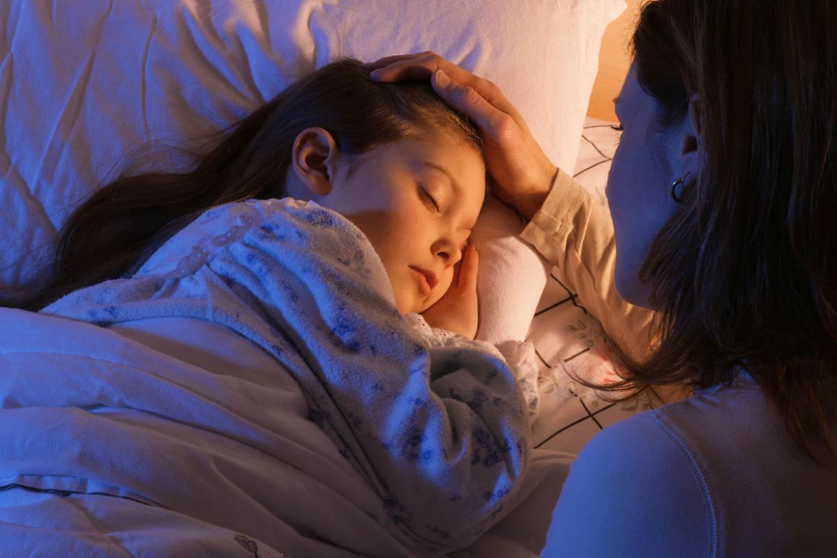Mother tucking her daughter into bed.