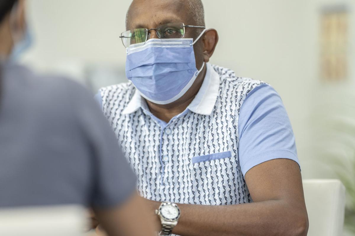 An African-American man wearing a mask talking to an unseen person in the foreground.