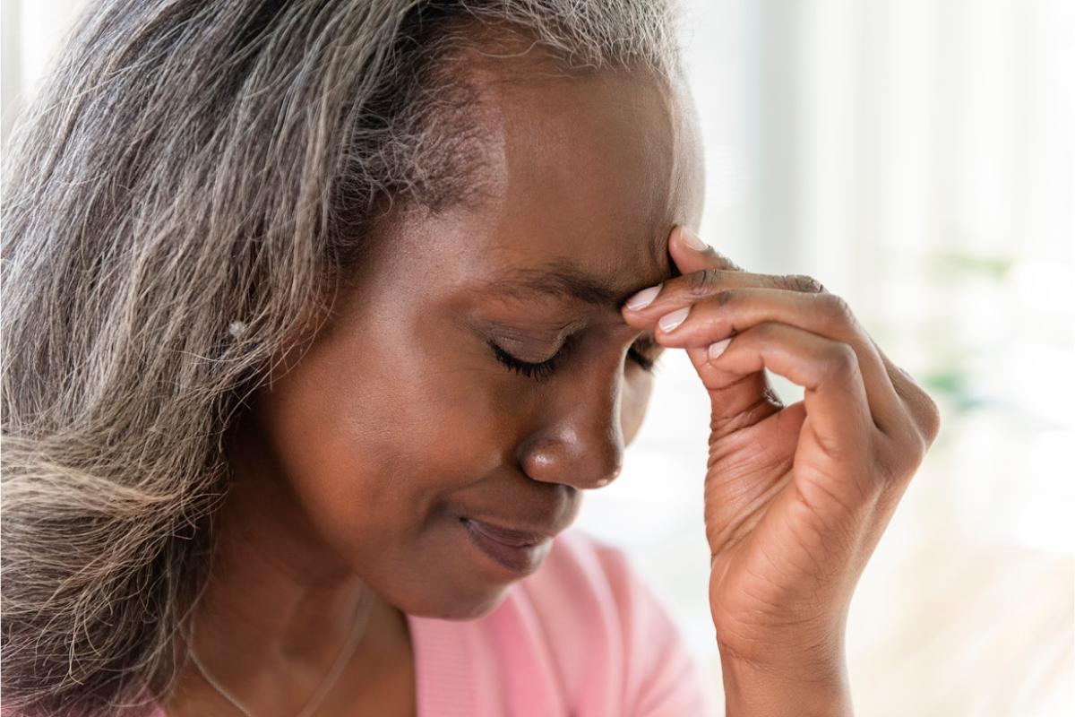 Close-up of an African-American woman, eyes closed, with her hand against her forehead.