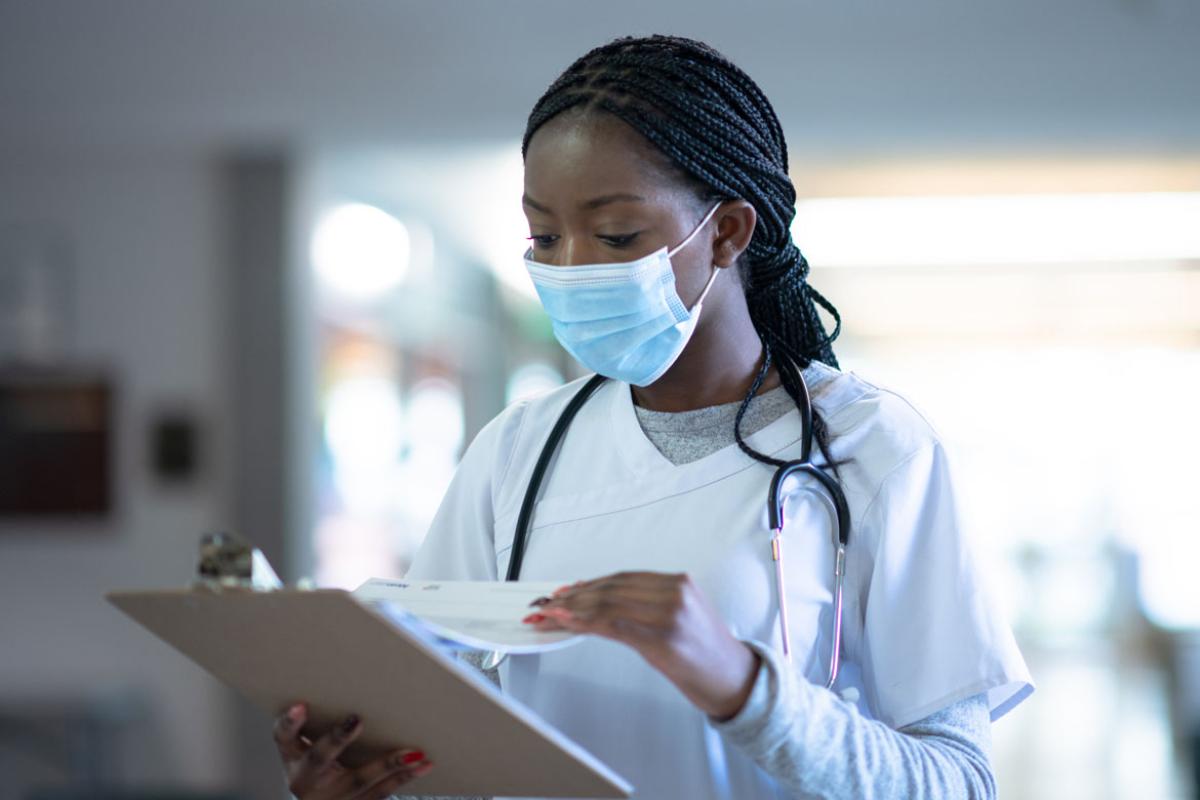 A masked doctor checking information on a clipboard.