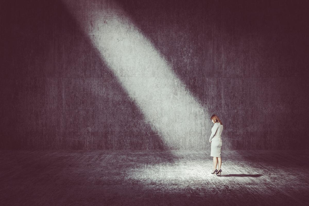 Woman in a suit standing in a dark room under a shaft of light.