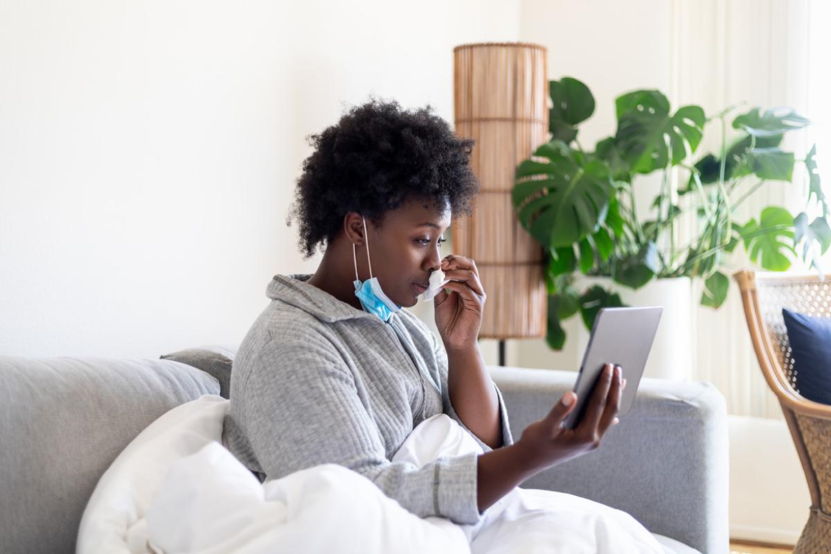African-American woman wearing a pulled down mask looking at a smart tablet.