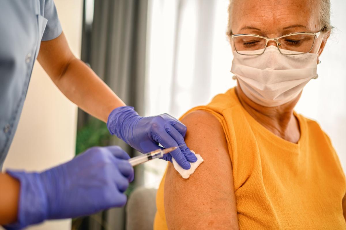 Woman wearing glasses and a mask being vaccinated by a slightly off-frame health care worker.
