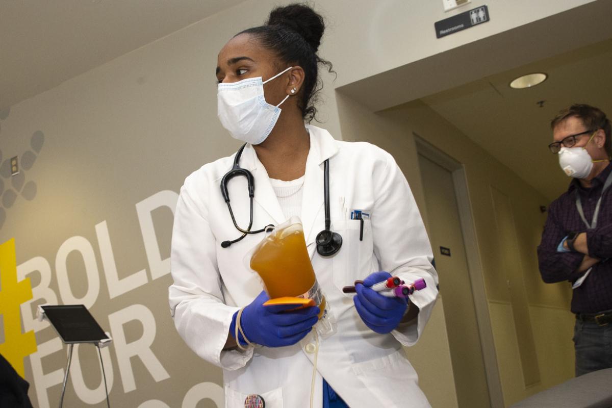 Doctor standing in hospital corridor wearing scrubs and PPE, holding vials