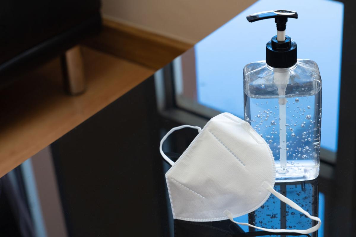 A desk with a PPE face mask and bottle of hand sanitizer.