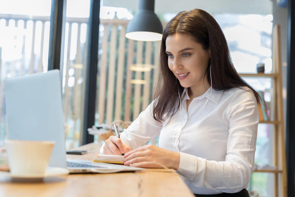 A woman with dark hair working at a laptop while wearing ear buds.