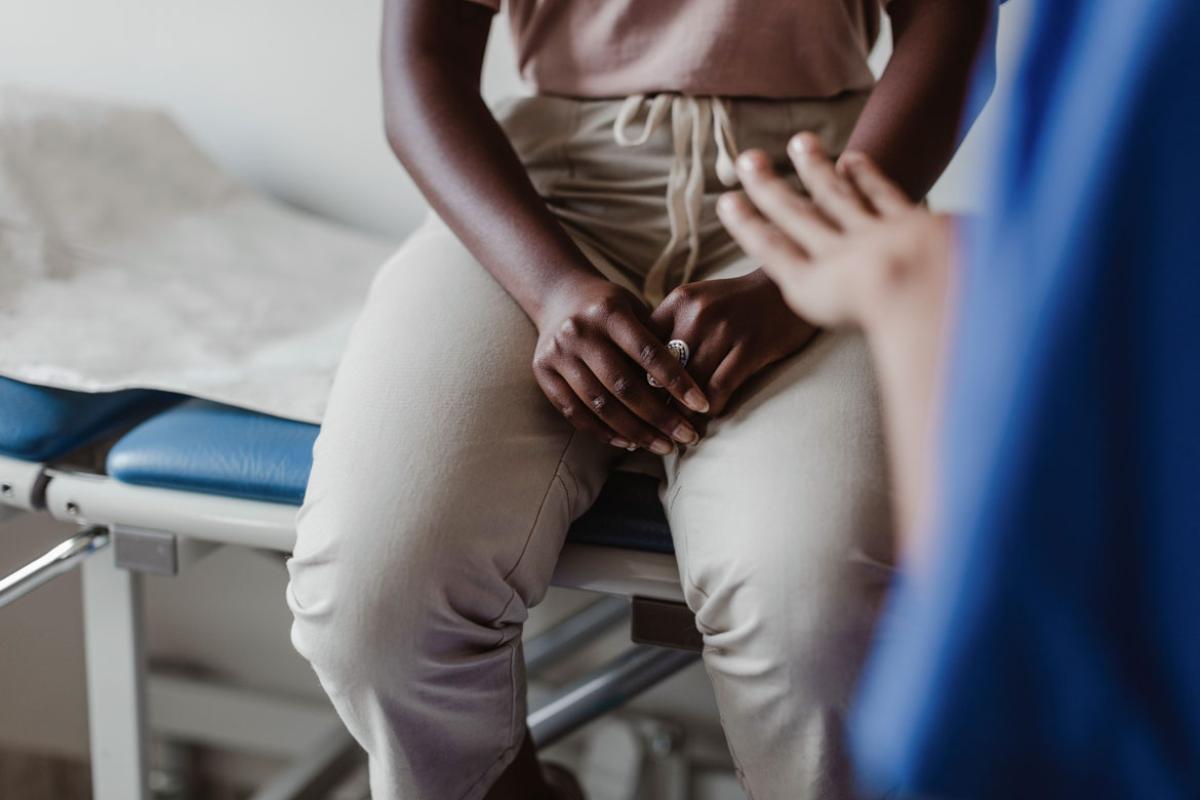 An African-American patient sitting on an examination table in the background with a health care working in the far right of the foreground.