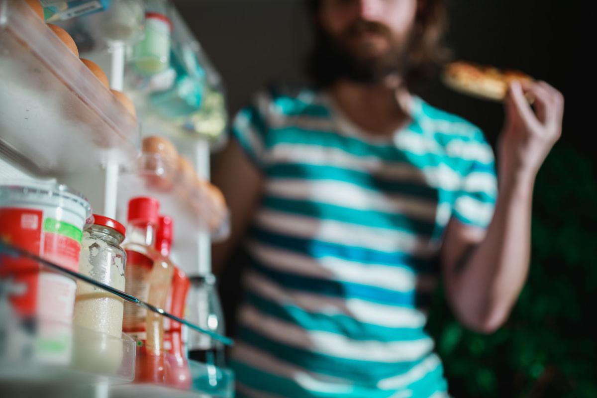 A bearded man opening a refrigerator, seen from the point of view of inside the refrigerator, with the side shelves and items in view.  