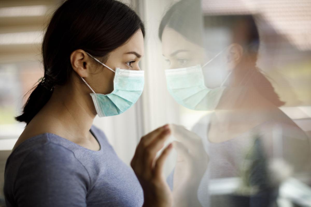 Woman with a mask, looking at her reflection through a window