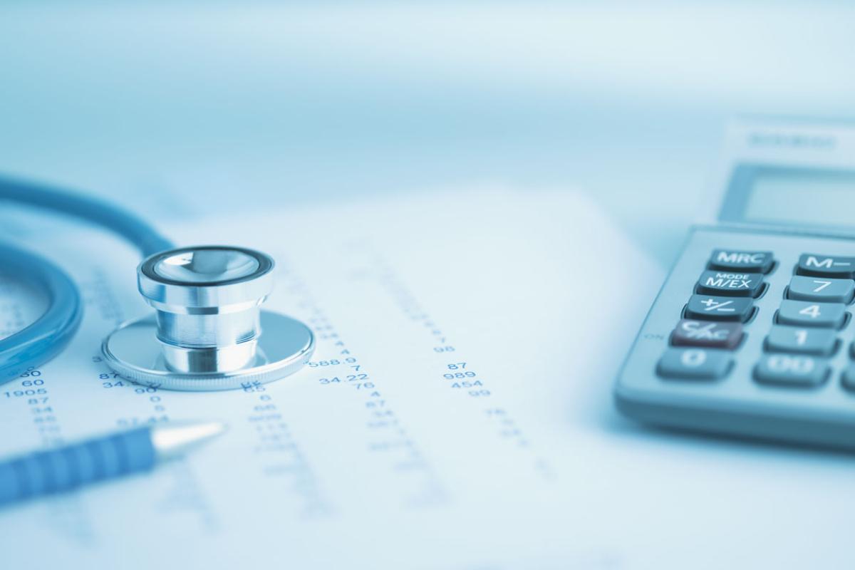Close-up of a stethoscope and a calculator sitting on a spreadsheet; the entire image is slightly tinted blue.