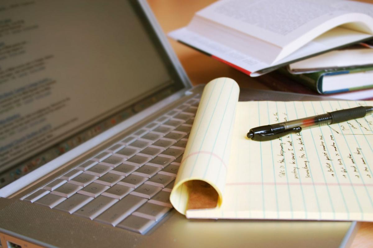 Photo of an open laptop with text on the screen with a yellow legal pad on top of the keys.