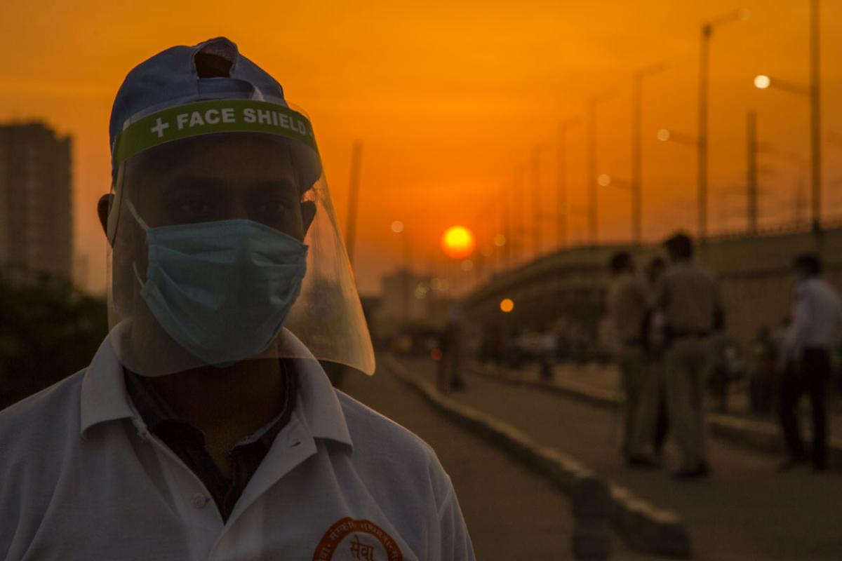 Crisis worker in full PPE in the foreground with people standing behind him as the sun sets.