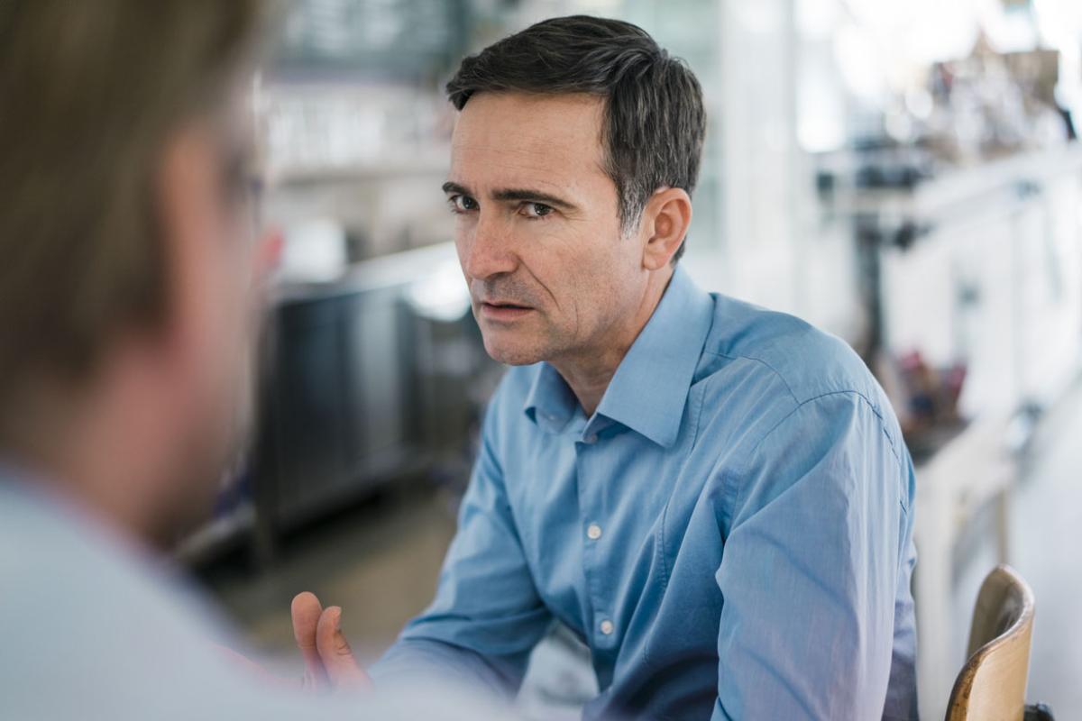 Worried patient in blue shirt sitting down talking to a physician.