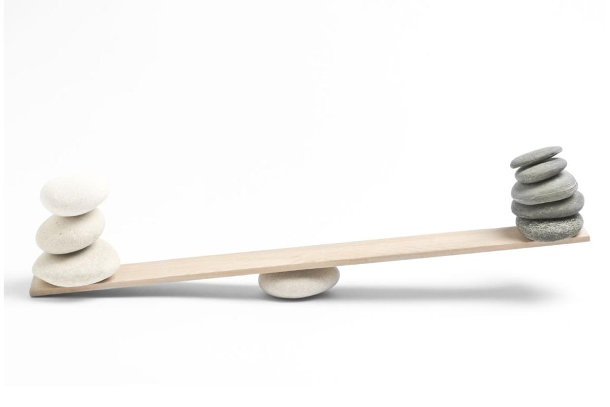 A see-saw made out of a plank and a white stone; on the left side, weighing down the see-saw, are three flat white stones while on the left side, in the air, are five flat dark grey stones.