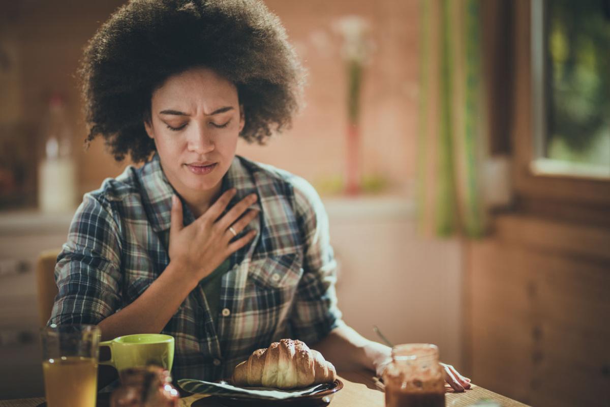 Person sitting at the breakfast table, eyes closed and holding a hand to their sternum.