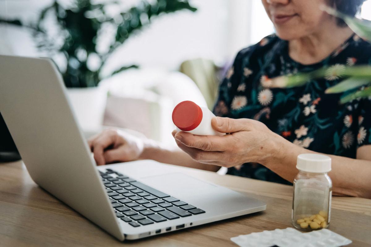 Person holding a prescription in front of a laptop