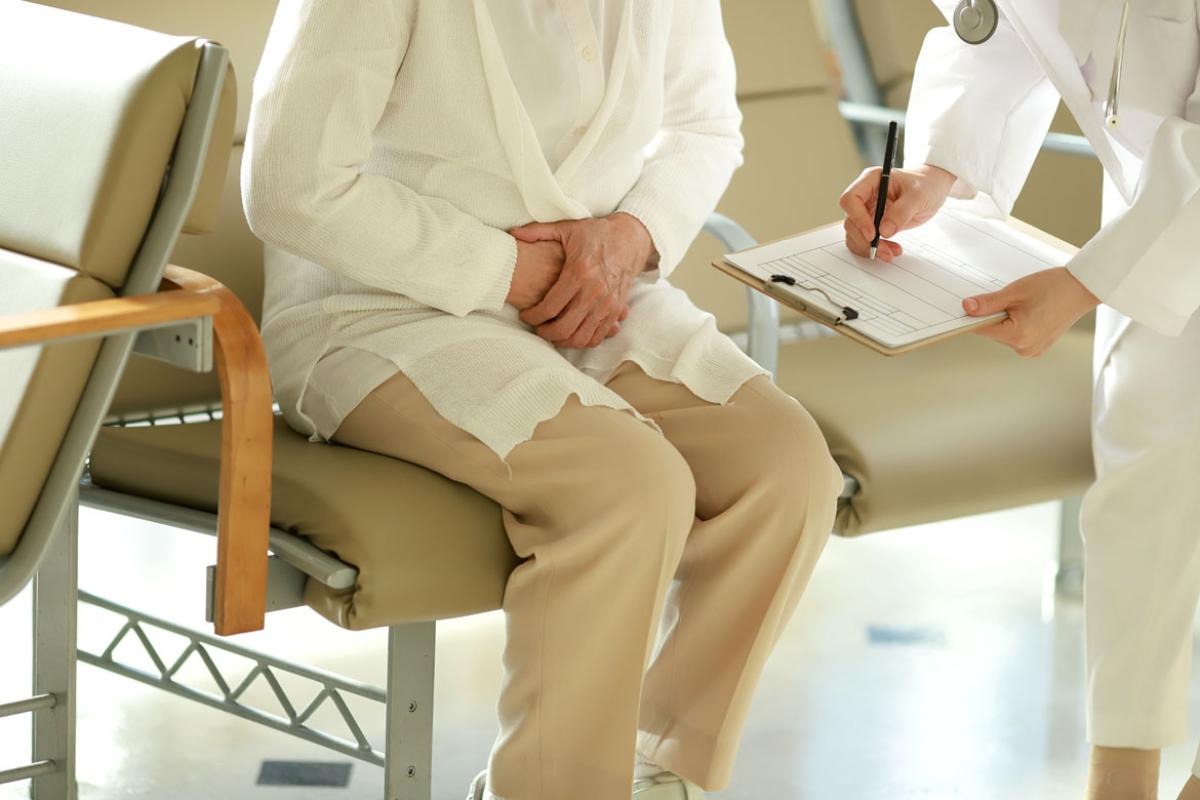 A patient and doctor, shown from the torso down, with the doctor handing a clipboard to the seated patient.