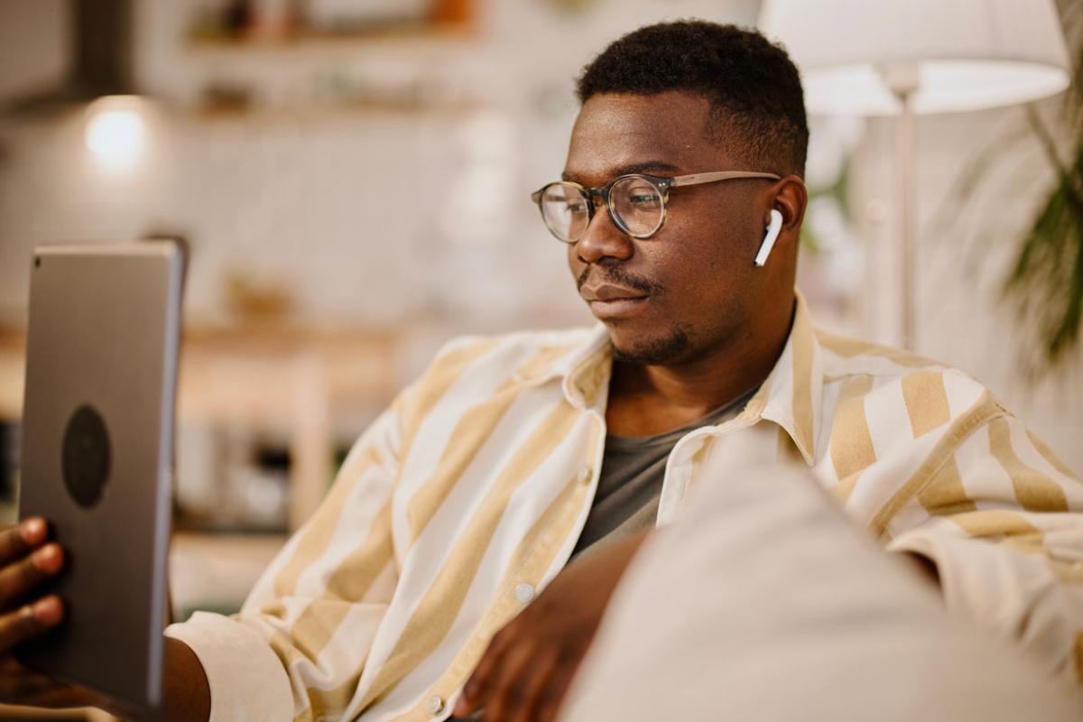 Person sitting on a sofa wearing wireless earbuds listening to something on a tablet.