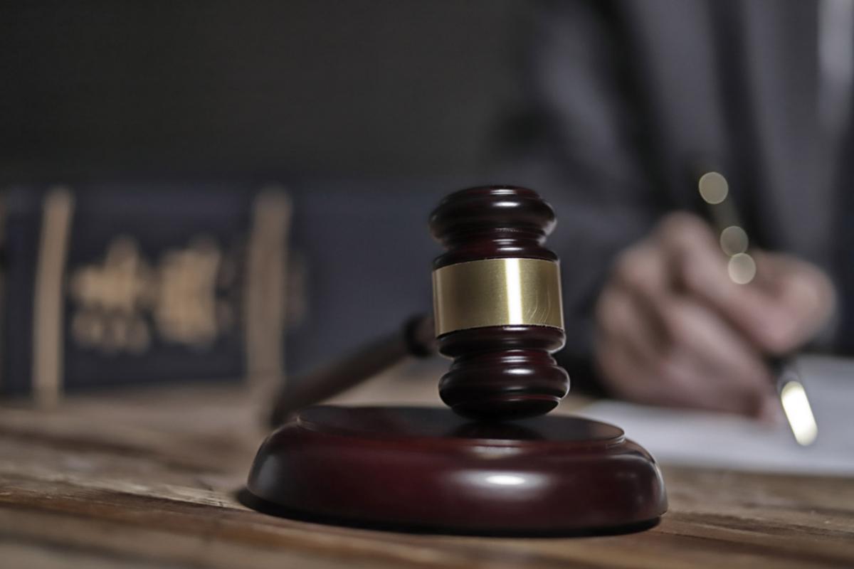 Close-up of a judge's gavel with a blurred out judge writing in the background.