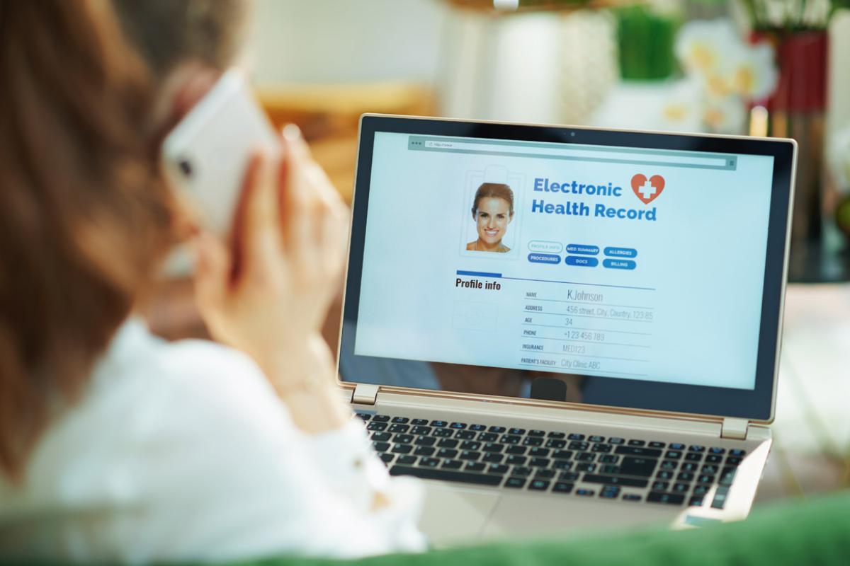 Person talking on cell phone and looking at computer screen displaying an electronic health record.