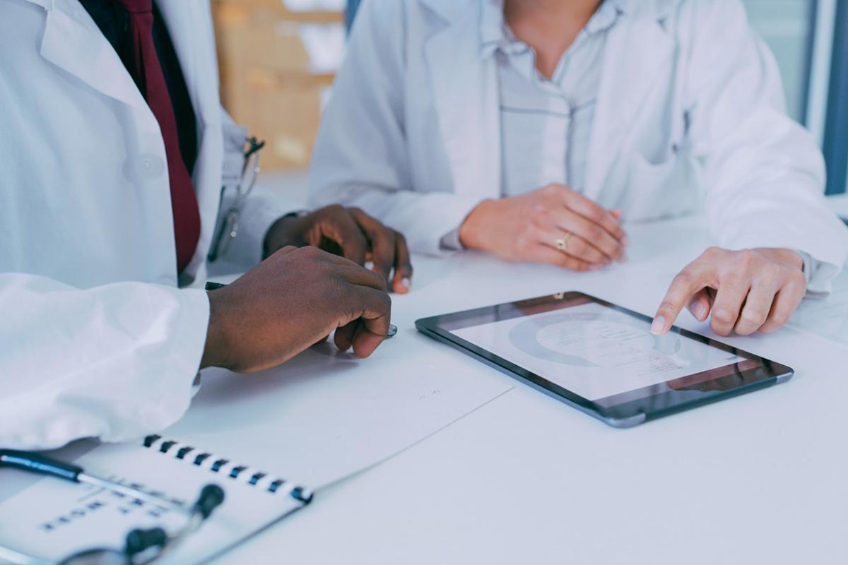Close up of two physicians reviewing patient medical information or medical research on a pad.