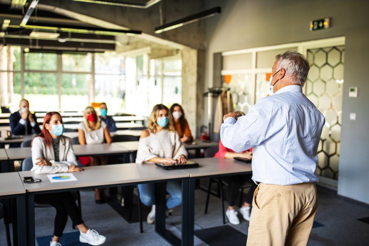 Man making a presentation in front of a group of college age people, all wearing masks