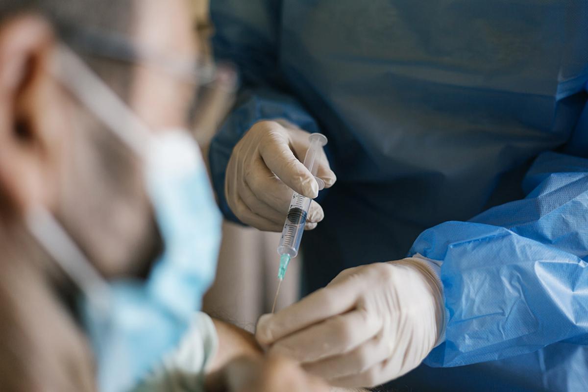 Close up of syringe with vaccine and health professional giving patient a shot